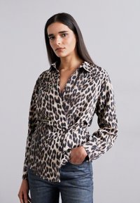 Camicia button-up con stampa leopardata in tessuto morbido, dotata di colletto, design avvolgente e maniche lunghe. Abbinata a jeans blu.
