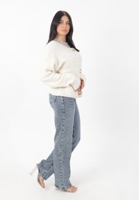 Cardigan cremoso con una texture a coste e tre grandi bottoni, abbinato a jeans azzurri e sandali con tacco trasparente. Design semplice e classico.
