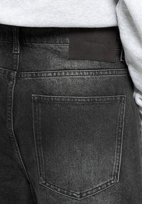 Jeans din denim negru cu o textură ușor decolorată. Dispune de o etichetă rectangulară din piele cu text embosat pe spate și un buzunar lateral.