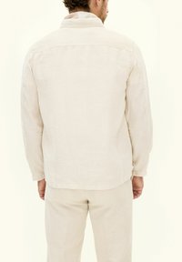 Camicia di lino beige con colletto, maniche lunghe e vestibilità comoda, caratterizzata da un orlo dritto e dettagli di cucitura visibili sul retro.