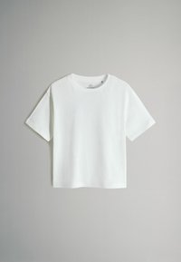 Camiseta blanca de algodón con cuello redondo, mangas cortas y un ajuste holgado. Textura suave, sin patrones ni gráficos.