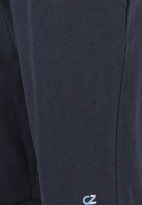 Tummansiniset puuvillaiset verkkahousut, joissa on pehmeä rakenne. Lahkeessa on pieni vaaleansinen logo ja klassinen kapeneva muotoilu.