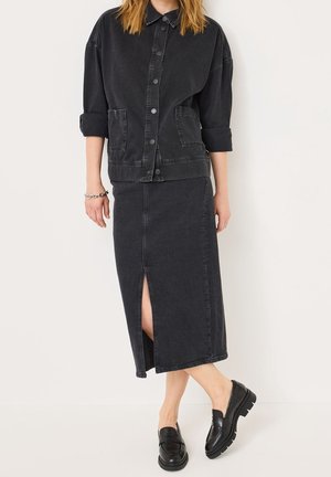 Veste en denim noir avec un col et deux poches avant, assortie d'une longue jupe en denim noir avec une fente sur le côté. Des mocassins noirs complètent le look.