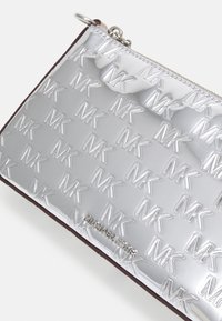 Clutch metallico argento con motivo a rilievo del logo MK, bordatura marrone a contrasto e chiusura con zip, design compatto per gli oggetti essenziali.