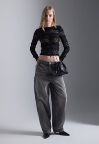 Black lace top with long sleeves, gray wide-leg jeans, and a small black bag. Pointed black heels complete the outfit.