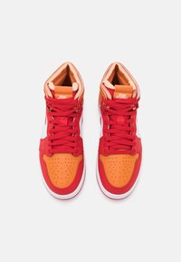 Paire de baskets montantes avec des lacets rouges, des embouts orange et des panneaux latéraux blancs, vues de dessus sur un fond blanc.