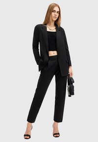 Blazer nero su un top nero corto e pantaloni a vita alta abbinati, caratterizzati da una texture liscia e un design minimalista.