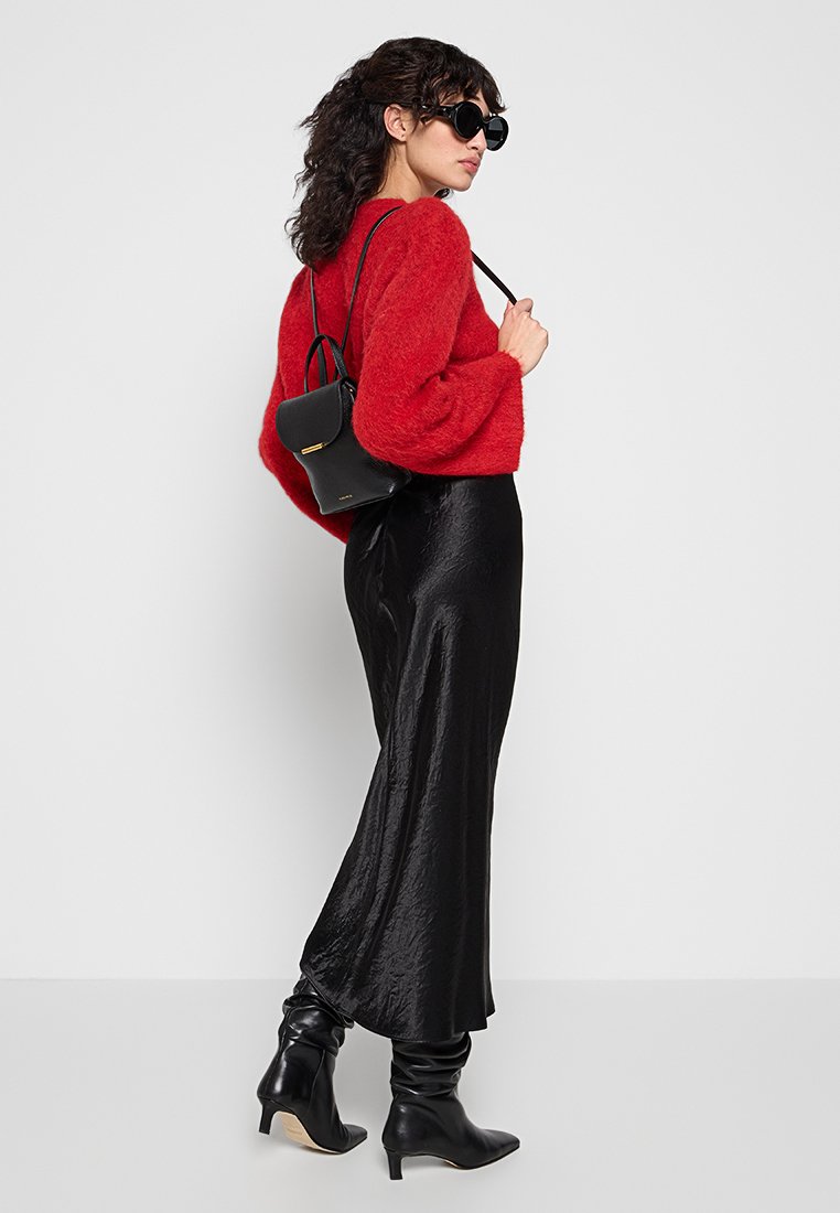 Czerwony puszysty sweter, czarna satynowa maksiówka, czarne buty za kolano oraz mała czarna torebka; modelka nosi duże czarne okulary przeciwsłoneczne.