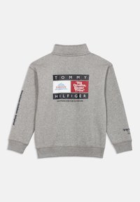 Γκρι φούτερ με ψηλό γιακά. Περιλαμβάνει γραφικά σχέδια σε πολλαπλά χρώματα στη πλάτη και κείμενο κατά μήκος του αριστερού μανικιού. Υλικό από μείγμα βαμβακιού.