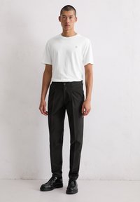 Witte katoen crew neck t-shirt gecombineerd met zwarte broeken met een voorknop en elastische tailleband, aangevuld met zwarte veterschoenen.