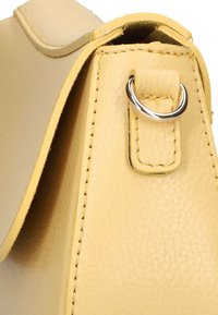 Gele leren tas hoek met zichtbare stiksels, een zilveren metalen ring aan een band, en een gladde textuur. Eenvoudig, hoekig ontwerp.