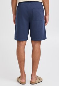 Tamsiai mėlyni šortai iš minkštos medžiagos, su galine kišene, elastinga juosmens dalimi ir apdailintais kraštais, derinami su kasdieniais bateliais be užsegimo.