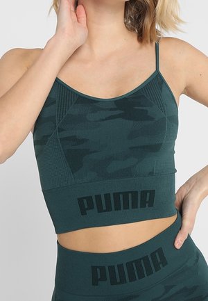 Femme portant un crop top et un legging Puma à motif camouflage vert foncé, avec le logo Puma sur les deux vêtements.