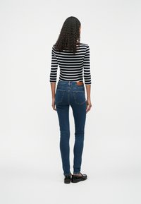 Λεπτά �τζιν σε σκούρο μπλε ντένιμ με ελάχιστη φθορά, συνδυασμένα με μπλούζα με μαύρες και λευκές ρίγες. Διαθέτουν δερμάτινη λεπτομέρεια στη μέση.