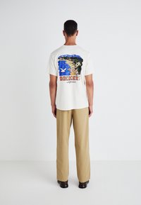 White cotton t-shirt featuring a colorful graphic design on the back with "DOCKERS California" text, paired with tan trousers.