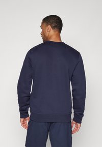 Sweat-shirt bleu marine en tissu doux, avec des manches longues, un col rond et un ourlet côtelé. Texture lisse sans motifs visibles.
