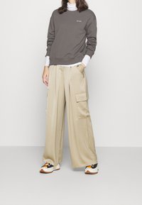 Grå sweatshirt med vit logotyp, beige vida cargobyxor med sidofickor och sportiga svarta och orange sneakers. Släta texturer synliga.