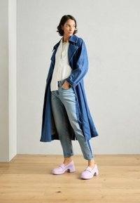 Denim trenchcoat, ljusblå jeans och lila klackskor med grova sulor. Grov textur, bred krage och långa ärmar med blå detaljer.