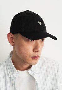 Black baseball cap made of cotton, featuring a small silver heart emblem on the front. Soft texture, curved brim, and six-panel design.