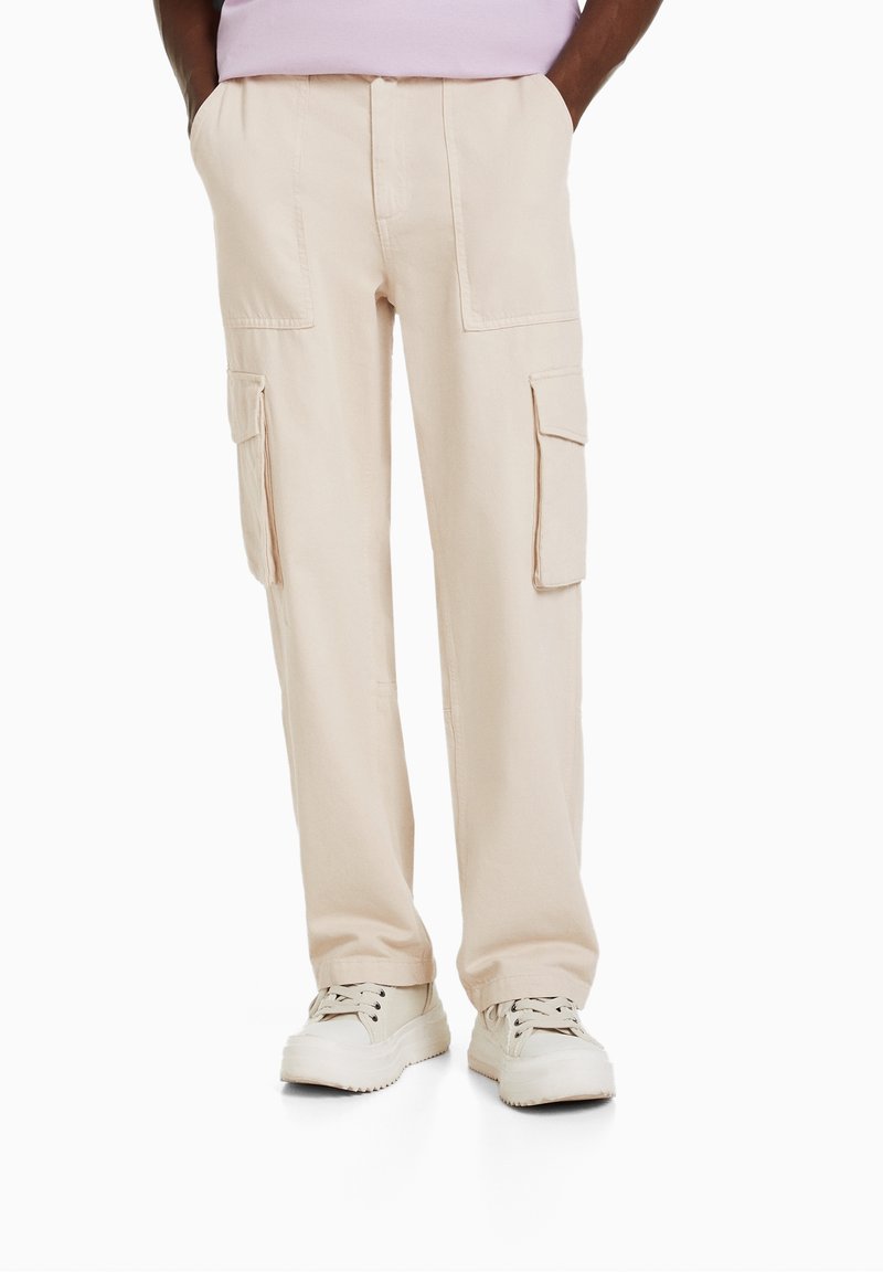 Beige cargo kalhoty se dvěma bočními kapsami a dvěma předními cargo kapsami. Vyrobené z odolného materiálu, volný střih a rovné nohavice.