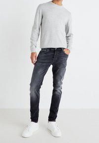 Pull gris avec col rond, associé à un jean gris foncé avec un effet délavé. Des baskets blanches complètent la tenue.