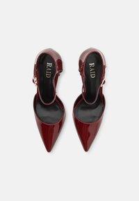 Tacchi slingback in pelle lucida bordeaux con punte appuntite e interno nero. Presentano una fascia con fibbia regolabile. Il nome del brand "RAID" è ben visibile.