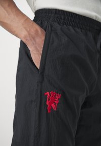 Černé lehké kalhoty s elastickým pasem, na přední kapse mají vyšívaný červený emblém. Texturovaná tkanina s hladkým povrchem.