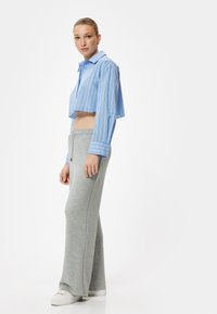 Blaustripes Hemd mit weit geschnittenem Kragen und langen Ärmeln, kombiniert mit hellgrauen Jogginghosen. Weiße Sneakers runden das Outfit ab.