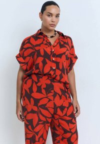 Red and brown patterned shirt with short sleeves, buttoned front, and relaxed fit. Paired with matching trousers featuring similar floral design.