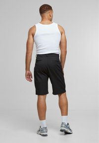 Shorts noirs avec une texture lisse, dotés d'une taille standard et de deux poches arrière, associés à un débardeur blanc et des chaussures de sport.