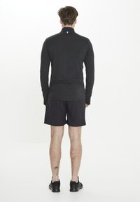 Langdurige mouw, donkergrijze sporttop met een hoge kraag, gecombineerd met zwarte shorts. Beschikt over een platte naadontwerp en een subtiel logo bij de hals.