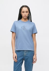 Lys blå bomulls-T-skjorte med korte ermer og rund hals. Har en liten brodert "cK"-logo på brystet. Klassisk passform.