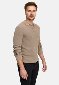 Pullover in maglia beige con texture, dotato di patta con tre bottoni, maniche lunghe e design aderente. Abbinato a pantaloni neri.