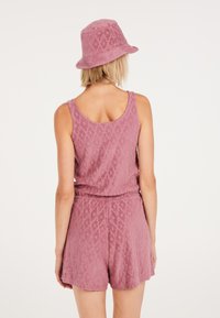 Ensemble deux pièces rose clair en tissu texturé, composé d'un haut sans manches et de shorts. Comprend un chapeau seau assorti.