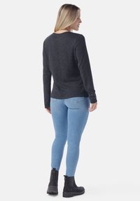 Schwarzes, geripptes Langarmshirt, kombiniert mit hellblauen Skinny Jeans und schwarzen Knöchelstiefeln, von hinten vor einem weißen Hintergrund gezeigt.