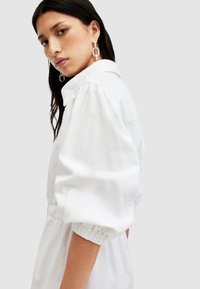 Weißes Baumwollkleid mit Kragen, Puffärmeln und elastischen Bündchen. Es hat eine lässige Passform und eine glatte Textur.