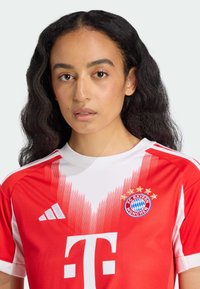 Punainen ja valkoinen FC Bayern Münchenin jalkapallopaita, jossa on liukuväri, lyhyet hihat, pyöreä pääntie, logo rinnassa ja kolme raitaa olkapäillä.