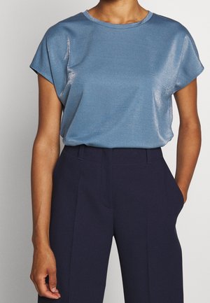 Světle modrý top s krátkým rukávem vyrobený z lesklé tkaniny s kulatým výstřihem, zkombinovaný s tmavě modrými kalhotami s vysokým pasem. Hladká textura, uvolněný střih.