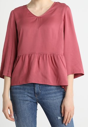 Rosa V-Ausschnitt-Bluse mit drei Viertel-Bellärmeln, geraffter Taille und einem glatten, leichten Stoff. Kombiniert mit verwaschenen Jeans.