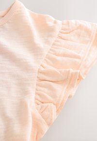 Lyserød ferskenfarvet bomulds-T-shirt med rund halsudskæring. Har et flæsedetalje på ærmet og en blød, tekstureret finish.
