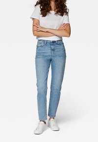 Vaqueros de talle alto azul claro con un ajuste slim y un ligero elastano. Combinados con una camiseta blanca lisa y deportivas blancas.