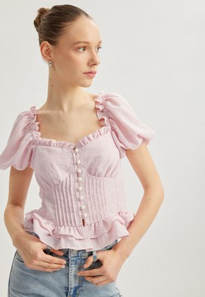 Rosa Leinenbluse mit Puffärmeln, gerafftem Ausschnitt und Knopfleiste mit weißen Knöpfen. Taillierte Passform mit ausgestelltem Saum.