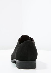 Chaussure en velours noir avec un bout arrondi, un petit talon et une semelle noire lisse. Présente un design simple et épuré sans matériel visible ni motifs.