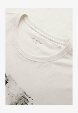 T-shirt blanc à col rond avec étiquette de marque "ombre" et design graphique partiel avec texte noir et gris à l'avant.