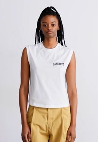Valge õlavabadega puuvillane topp, millel on ümar kaelus ja rindadele tikitud "Carhartt" logo, kombineeritud kollaste kõrge talje jaotustega pükstega.