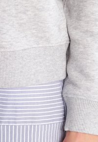 Tela de sudadera gris claro con un acabado texturizado, que presenta puños y dobladillo acanalados. Combinado con una falda a rayas en lavanda y blanco.