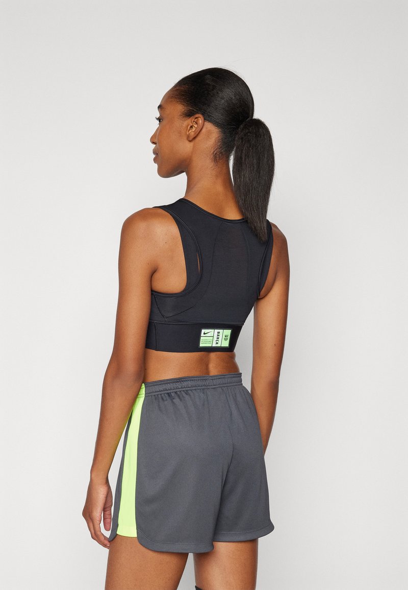 Reggiseno sportivo nero con design racerback, caratterizzato da un piccolo etichetta verde. Abbinato a pantaloni corti grigi con una accentuazione verde neon sui lati.