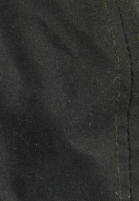 Black fabric texture with a slightly coarse finish, featuring visible green stitching along a seam. Fibers and lint visible on the surface.