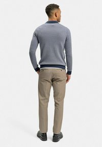 Grå texturerad stickad tröja med marinblå krage, tillsammans med beigefärgade slim-fit byxor och svarta skor, sedd bakifrån.