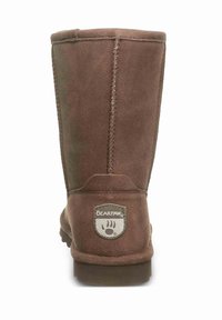 Braune Wildleder-Stiefel bis zur Wade mit genähten Nähten, Gummisohle und einem runden Logo-Patch mit einem Bärenpfotenmotiv auf der Rückseite.